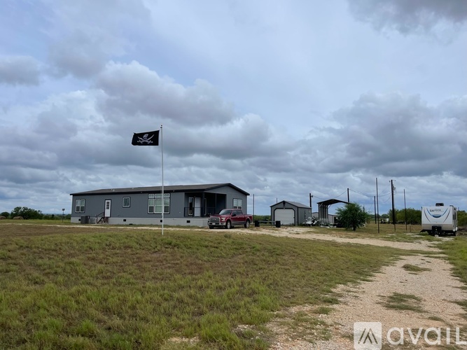 A flag with a black background and a white skull is on a pole in front of a grey building.