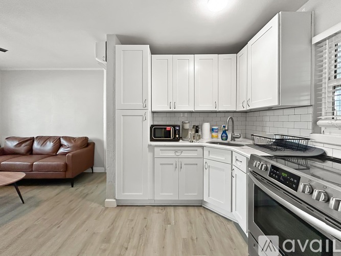 A kitchen with white cabinets and a brown leather couch.