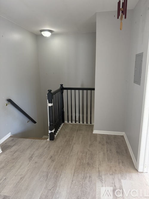 A room with a wooden floor and a staircase with black railings.