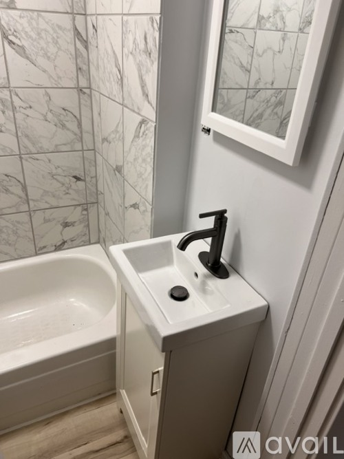 A white sink with a black faucet is mounted on a wall next to a bathtub.