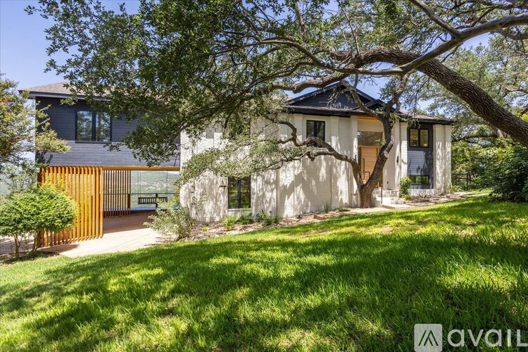 A house with a white exterior and a brown door is surrounded by greenery.