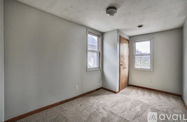 A room with a carpeted floor and two windows.