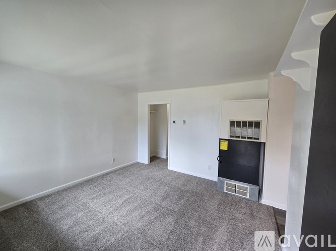 A room with a grey carpet and a white wall with a doorway leading to another room.