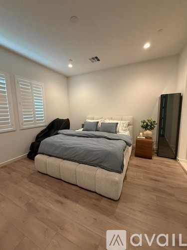 A bedroom with a bed, nightstand, and a plant.