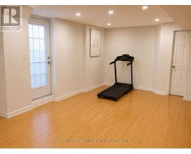 A treadmill is in the middle of a room with white walls and wooden flooring.