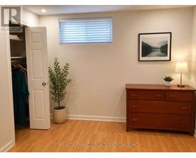 A room with a wooden floor, a white door, a dresser, a potted plant, and a framed picture on the wall.