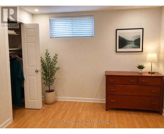 A room with a wooden floor, a white door, a dresser, a potted plant, and a framed picture on the wall.
