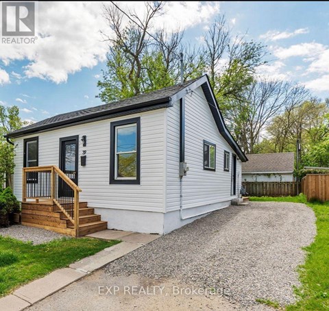 A small white house with a wooden deck and a gravel driveway.