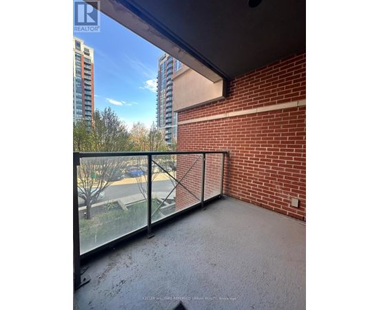 A balcony with a glass railing overlooking a parking lot and buildings.