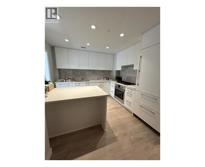 A modern kitchen with white cabinets and a wooden floor.