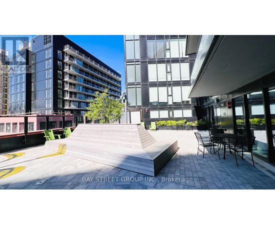A modern outdoor seating area with a bench and chairs is surrounded by contemporary buildings.