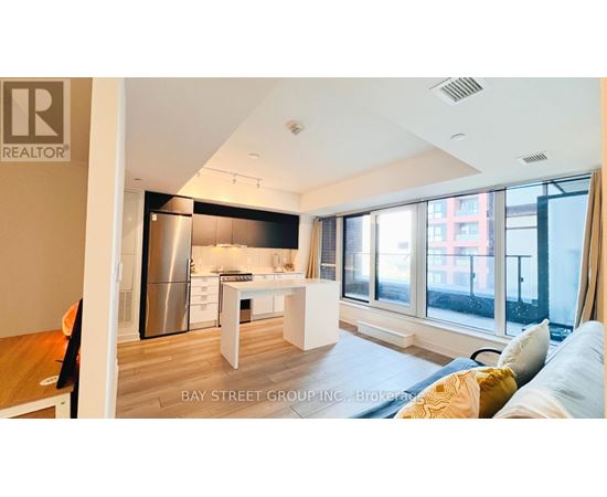A well-lit, modern kitchen with a dining table and chairs, and a living area with a sofa and a window overlooking a city street.