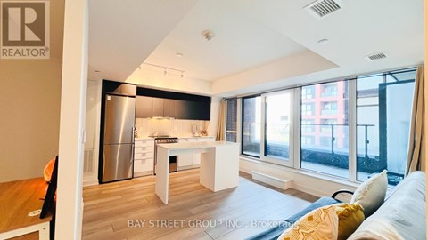 A well-lit, modern kitchen with a dining table and chairs, and a living area with a sofa and a window overlooking a city street.