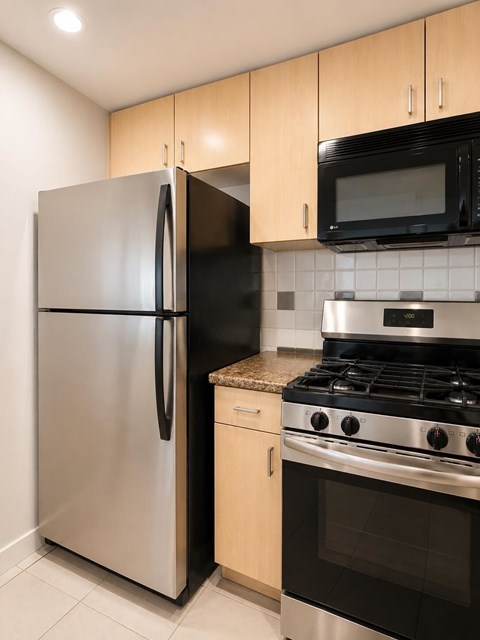 A kitchen with a stainless steel refrigerator and a black microwave above a stove.