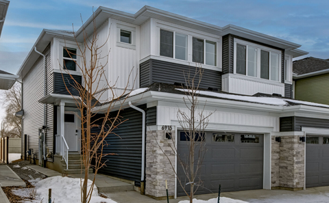A modern house with a grey and white exterior and a black garage door.