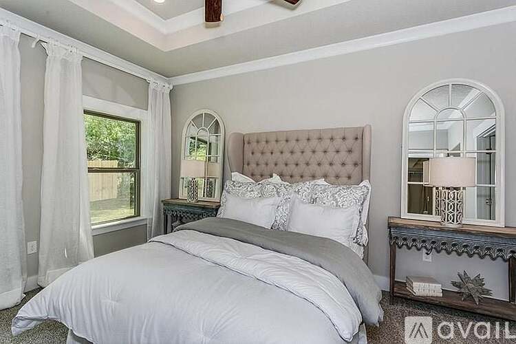 A bedroom with a large bed and a window with curtains.
