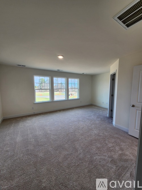 A room with a carpeted floor and a window with a view of a fence and trees.