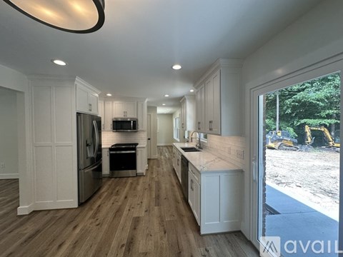A modern kitchen with white cabinets and a wooden floor.