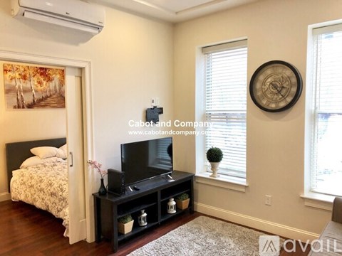 A bedroom with a bed, a television, and a window with blinds.