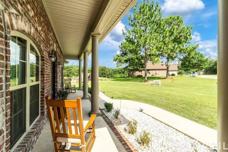 A wooden chair is on a porch with a view of a green lawn and trees.