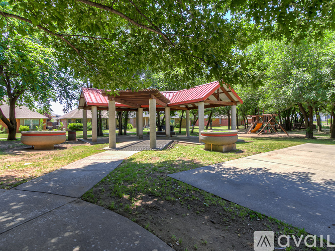 A gazebo with a red roof is surrounded by trees and has a concrete walkway leading to it.