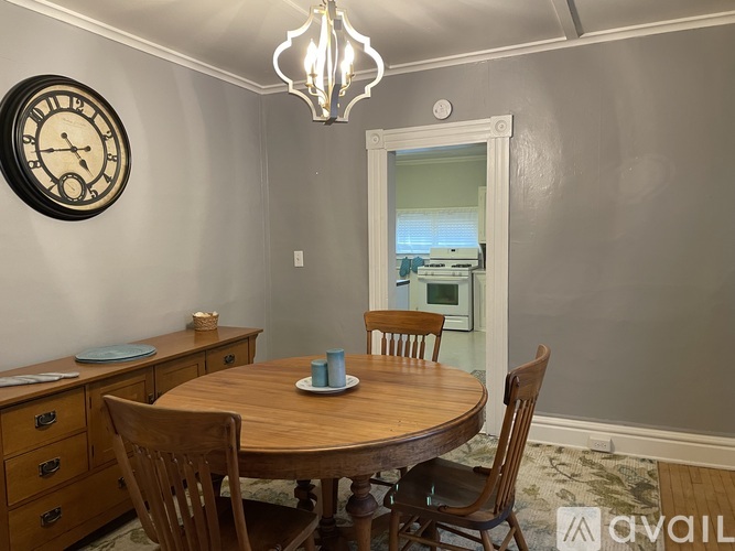 A dining room with a wooden table and chairs, a clock on the wall, and a chandelier hanging from the ceiling.
