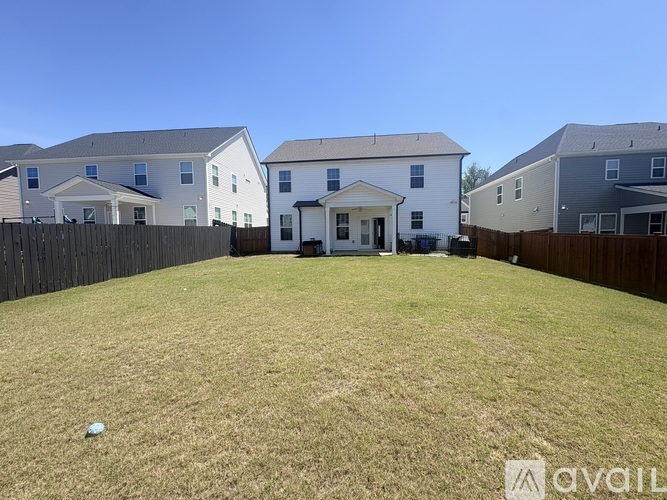 A grassy backyard with a white house in the middle and three other houses in the background.