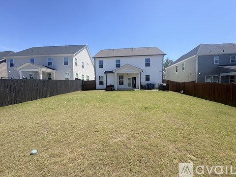 A grassy backyard with a white house in the middle and three other houses in the background.