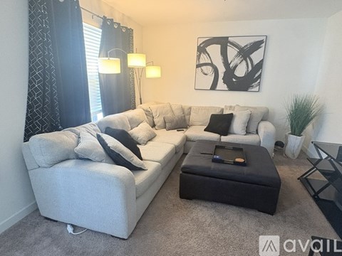 A living room with a grey couch, a black ottoman, and a large abstract painting on the wall.
