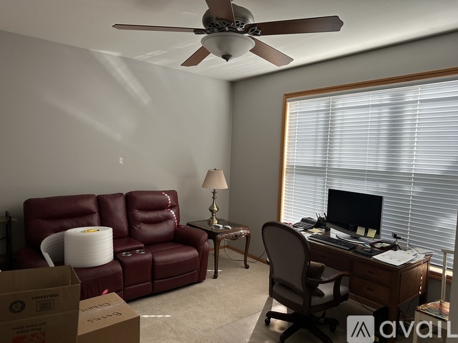 A room with a red leather couch, a desk with a computer, and a ceiling fan.