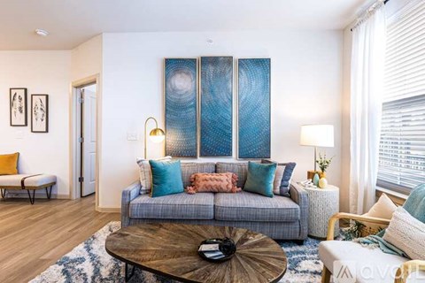 A living room with a grey couch, a coffee table, and a large abstract painting on the wall.