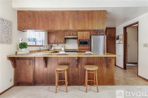 A kitchen with wooden cabinets and a countertop with two stools.