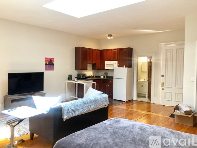 A bedroom with a bed, a television, and a kitchen area in the background.