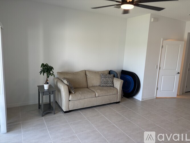 A living room with a beige couch, a small table with a plant, and a ceiling fan.