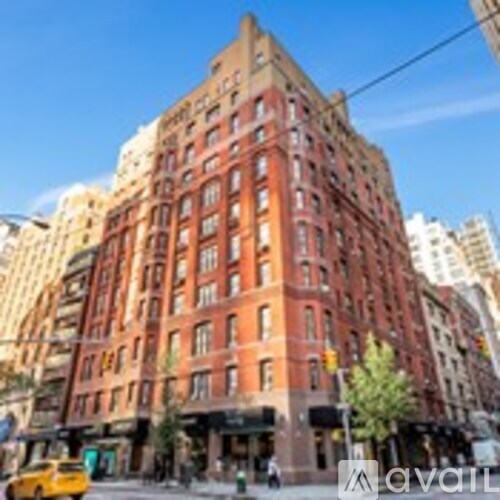 A tall red brick building with many windows and a yellow taxi in front.