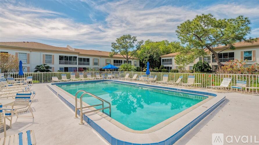 A pool surrounded by chairs and trees with apartment buildings in the background.