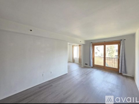 A spacious room with wooden flooring and a sliding glass door leading to a balcony.