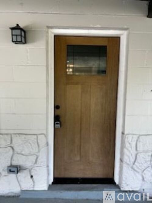 A brown door with a glass window is set in a white wall.