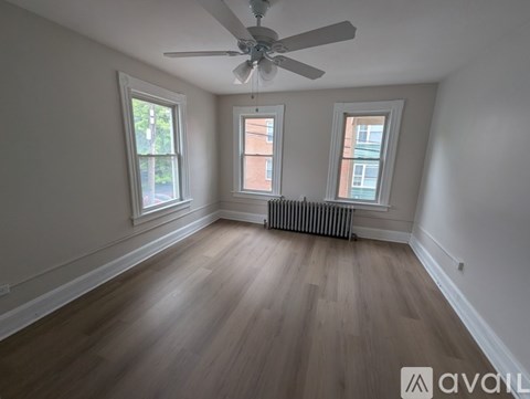 A room with a ceiling fan, two windows, and wooden flooring.