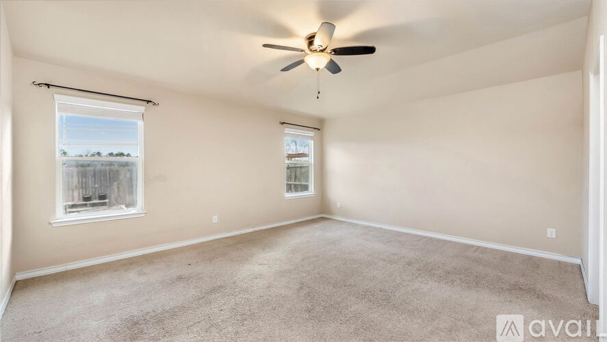 A spacious room with a ceiling fan and two windows.