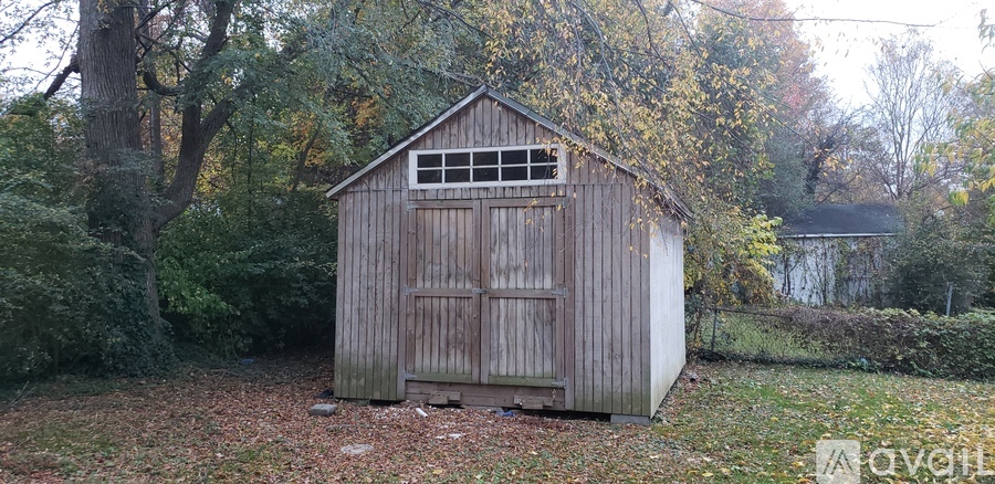 A shed sits in a grassy area surrounded by trees.