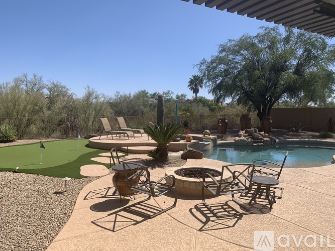 A patio with chairs and a table is surrounded by a gravel area and a green lawn.