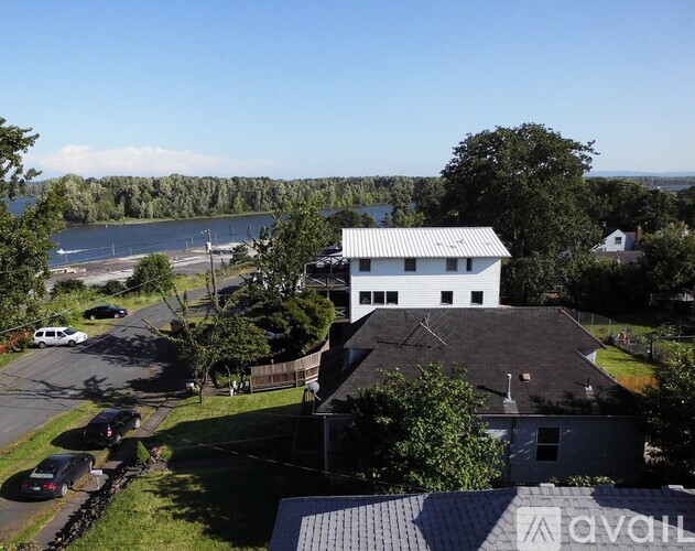 A house with a white exterior is surrounded by greenery and a body of water.