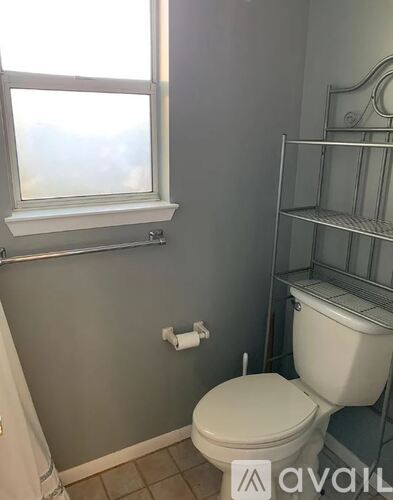 A white toilet in a bathroom with a window above it.