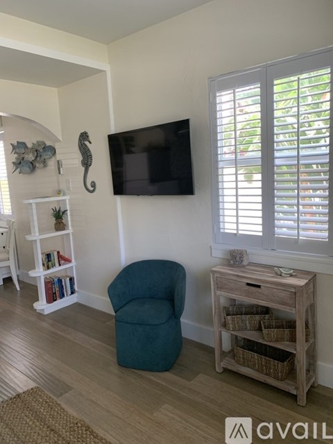 A living room with a blue chair, a white shelf with books, a flat screen TV, and a wooden table with baskets.
