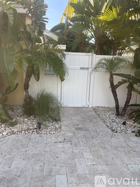 A white fence with a gate is surrounded by green plants and trees.