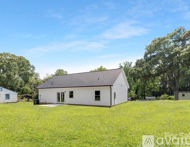 A white house with a black roof is surrounded by green grass and trees.