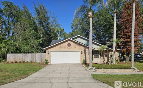 A house with a garage is surrounded by trees and has a driveway in front.