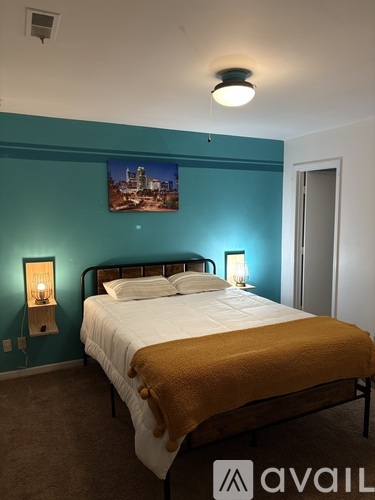 A bedroom with a bed, a nightstand with a lamp, and a picture on the wall.