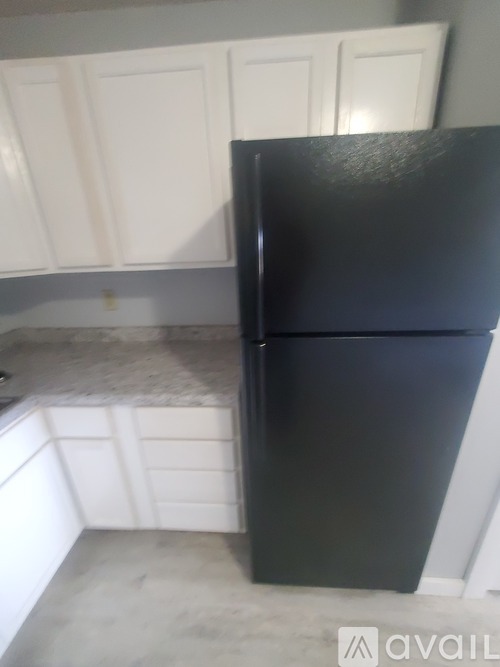 A black fridge in a kitchen with white cabinets.